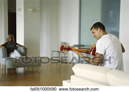 Man playing acoustic guitar in living room, woman watching View Large Photo Image Stock Image - Man playing acoustic guitar in living room, woman watching. Fotosearch