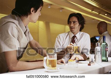 Man sitting at bar with friend, holding glass of beer View Large Photo Image Stock Image - Man sitting at bar with friend, holding glass of beer. Fotosearch