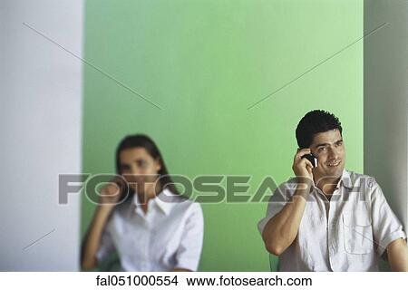 Man talking on cell phone, smiling, female in background View Large Photo Image Picture - Man talking on cell phone, smiling, female in background. Fotosearch