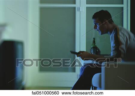 Man watching TV, holding beer and remote, side view View Large Photo Image Stock Image - Man watching TV, holding beer and remote, side view. Fotosearch