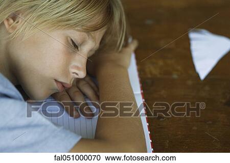 Stock Image - Preteen boy sleeping, resting head on arms laid across notebook. Fotosearch