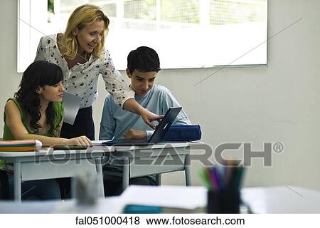 Teacher helping students using laptop computer in class View Large Photo Image Stock Photo - Teacher helping students using laptop computer in class. Fotosearch