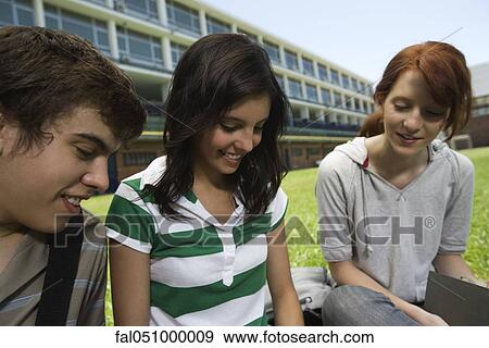 Stock Photo - Teenage friends hanging out, sitting together outdoors on school lawn. Fotosearch