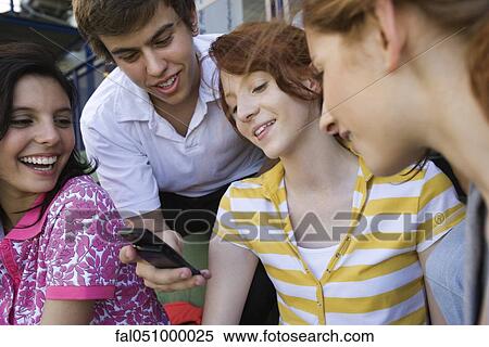 Teenage friends together, boy showing girl cell phone, others looking with amusement View Large Photo Image Stock Photography - Teenage friends together, boy showing girl cell phone, others looking with amusement. Fotosearch