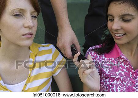 Teenage girl looking at cell phone handed to her by friend View Large Photo Image Stock Photograph - Teenage girl looking at cell phone handed to her by friend. Fotosearch