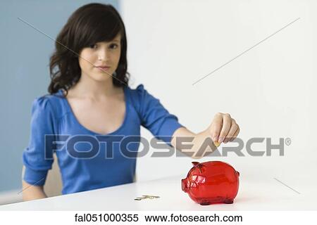 Stock Photography - Teenage girl putting coin in piggy bank. Fotosearch