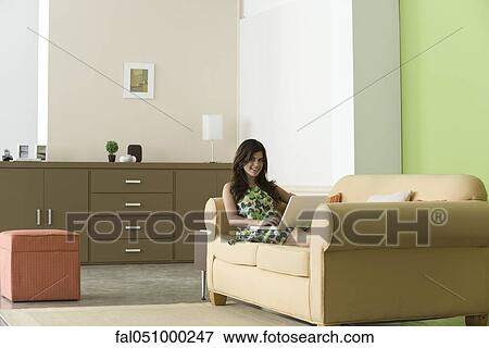 Stock Photo - Teenage girl relaxing on sofa using laptop in living room. Fotosearch