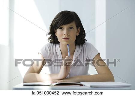Stock Image - Teenage girl sitting at desk, thinking, portrait. Fotosearch