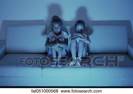 Two girls watching TV together on sofa at night View Large Photo Image Stock Photo - Two girls watching TV together on sofa at night. Fotosearch