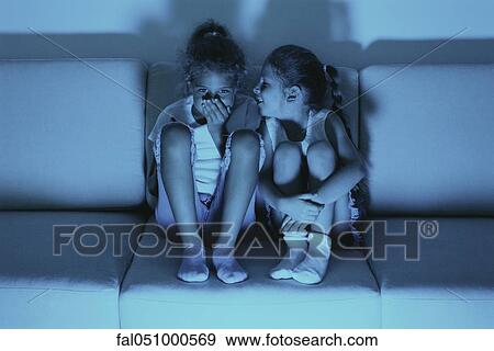 Two girls watching TV together, one whispering in the other's ear View Large Photo Image Stock Photo - Two girls watching TV together, one whispering in the other's ear. Fotosearch