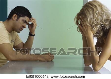Upset couple sitting at table, both holding heads View Large Photo Image Stock Image - Upset couple sitting at table, both holding heads. Fotosearch