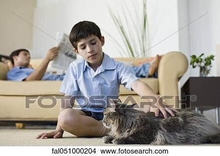 Young boy sitting in living room petting cat View Large Photo Image Picture - Young boy sitting in living room petting cat. Fotosearch