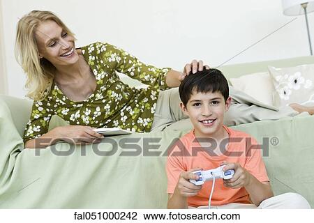 Young boy sitting on floor playing video game, mother relaxing on sofa View Large Photo Image Stock Image - Young boy sitting on floor playing video game, mother relaxing on sofa. Fotosearch