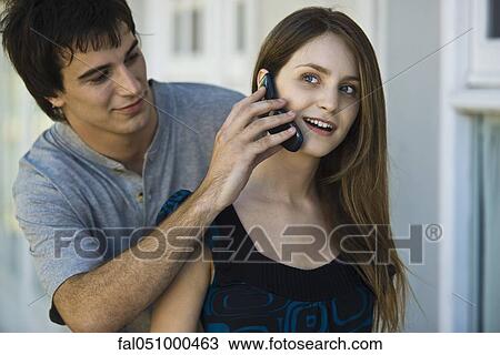 Stock Image - Young man holding cell phone to girlfriend's ear. Fotosearch