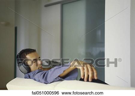 Young man listening to headphones, eyes closed View Large Photo Image Stock Photograph - Young man listening to headphones, eyes closed. Fotosearch