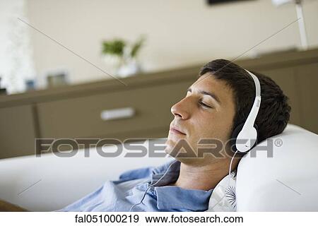 Young man relaxing on sofa listening to music with headphones View Large Photo Image Stock Photo - Young man relaxing on sofa listening to music with headphones. Fotosearch