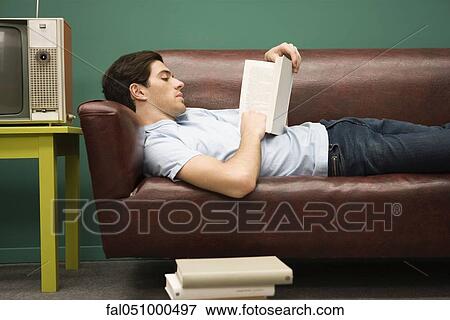 Young man relaxing on sofa with book View Large Photo Image Stock Photo - Young man relaxing on sofa with book. Fotosearch