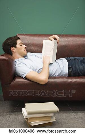 Stock Photograph - Young man relaxing on sofa with book. Fotosearch