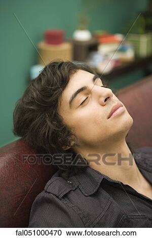 Young man resting on sofa with eyes closed View Large Photo Image Stock Image - Young man resting on sofa with eyes closed. Fotosearch