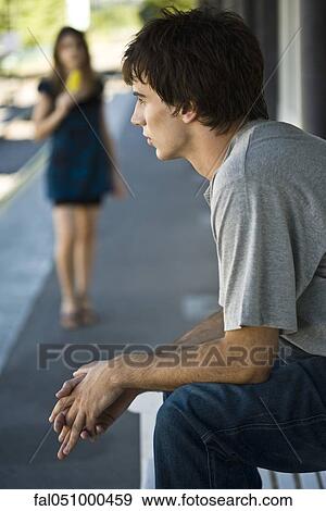 Stock Photo - Young man sitting on sidewalk bench. Fotosearch