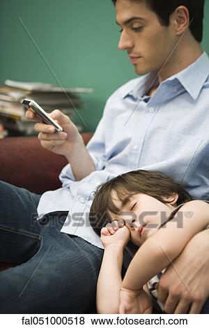 Young man text messaging while son naps with head in his lap View Large Photo Image Stock Photo - Young man text messaging while son naps with head in his lap. Fotosearch