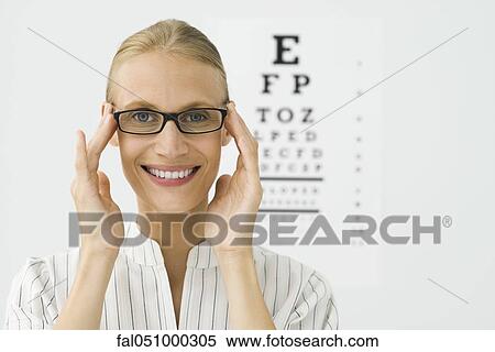 Young woman adjusting new glasses, eye chart in background, portrait View Large Photo Image Stock Photography - Young woman adjusting new glasses, eye chart in background, portrait. Fotosearch