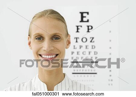Stock Image - Young woman, eye chart in background, portrait. Fotosearch