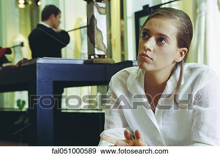 Stock Photo - Young woman looking up in thought, man in background. Fotosearch