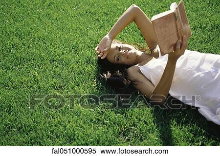 Young woman lying on grass, holding book, smiling at camera View Large Photo Image Stock Photography - Young woman lying on grass, holding book, smiling at camera. Fotosearch