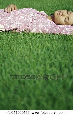 Stock Image - Young woman lying on grass with eyes closed. Fotosearch