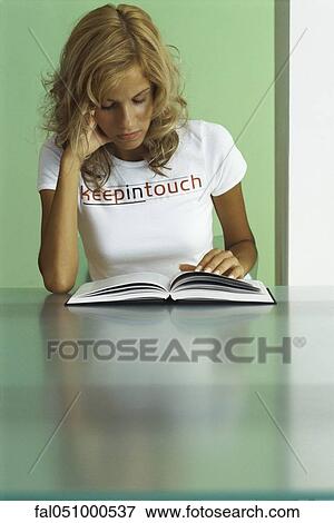 Stock Photo - Young woman reading book, wearing tee-shirt printed with &quot; keep in touch&quot;. Fotosearch