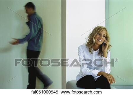 Young woman using cell phone, man walking in background, also on cell phone View Large Photo Image Stock Photography - Young woman using cell phone, man walking in background, also on cell phone. Fotosearch