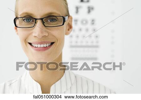 Young woman wearing glasses, eye chart in background, portrait View Large Photo Image Picture - Young woman wearing glasses, eye chart in background, portrait. Fotosearch