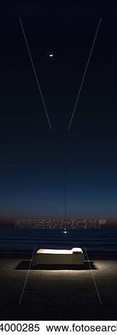 Stock Photography - Bed illuminated by hanging lamp on beach. Fotosearch