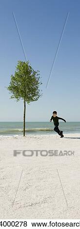 Stock Photo - Boy running around tree growing on beach. Fotosearch