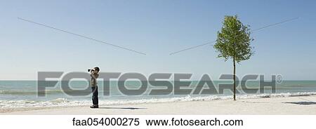 Stock Photography - Boy standing on beach, looking at sea with binoculars. Fotosearch