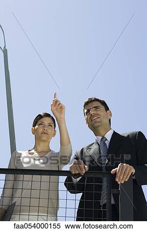 Stock Photography - Business associates on balcony looking at view, woman pointing. Fotosearch
