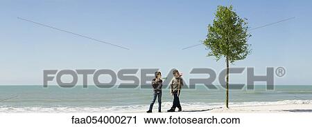 Stock Image - Children standing with gardening tools beside tree planted on beach. Fotosearch