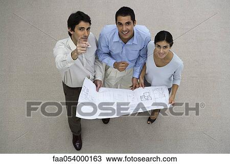 Stock Image - Colleagues holding blueprint, looking up. Fotosearch