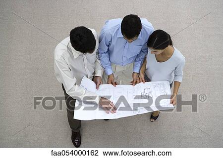 Stock Image - Colleagues looking at blueprint together. Fotosearch