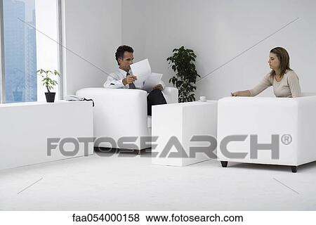 Stock Photo - Colleagues sitting together in office, man reviewing documents. Fotosearch