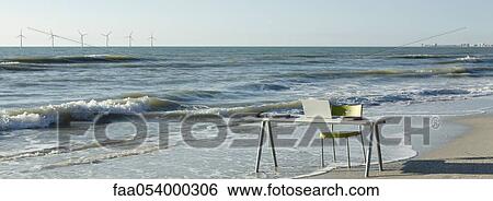 Desk and chair with laptop computer set at water's edge on beach, wind turbines on horizon View Large Photo Image Stock Photograph - Desk and chair with laptop computer set at water's edge on beach, wind turbines on horizon. Fotosearch