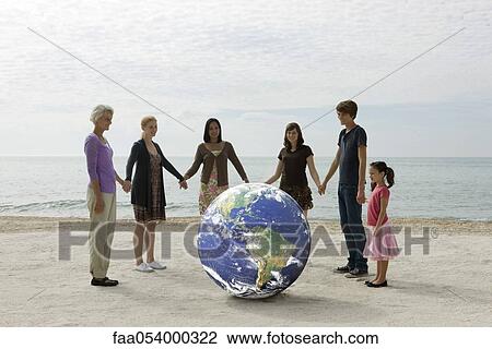 Stock Image - Ecology concept, group of people holding hands, standing around the planet earth. Fotosearch