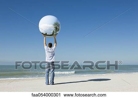 Stock Image - Holding aloft globe displaying image of trees. Fotosearch