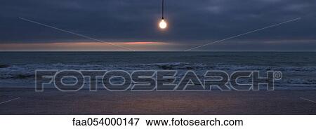 Stock Photo - Light bulb illuminated over beach at sunset. Fotosearch