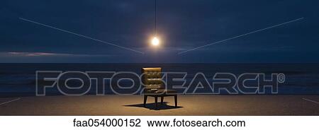 Stock Image - Light bulb illuminated over chair on beach at night. Fotosearch