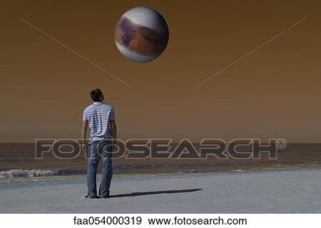 Man on beach looking up at alien world orbiting overhead against brown sky View Large Photo Image Stock Photo - Man on beach looking up at alien world orbiting overhead against brown sky. Fotosearch