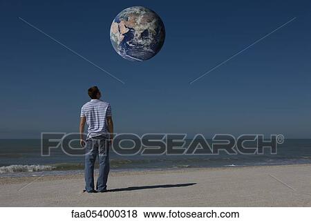 Man on beach looking up at planet earth orbiting overhead View Large Photo Image Stock Photo - Man on beach looking up at planet earth orbiting overhead. Fotosearch