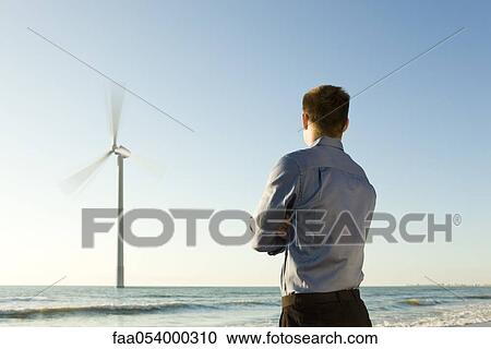 Man on beach observing offshore wind turbine at work View Large Photo Image Stock Image - Man on beach observing offshore wind turbine at work. Fotosearch