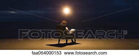 Stock Image - Man sitting in chair under light bulb on beach at night, reading book. Fotosearch
